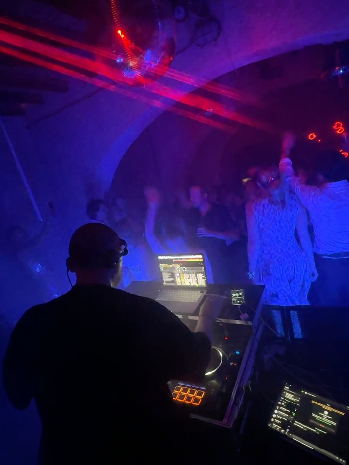 Andrew Mackenzie DJ mixing in a vaulted nightclub while the crowd dances under purple light